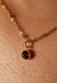 Goldkettchen mit einem runden, facettierten Granatanhänger. Die Kette hat verbundene ovale Formen und kleine runde Akzente.