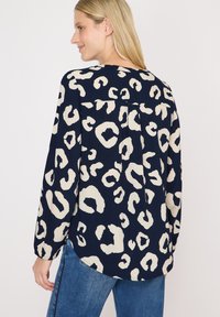 Marineblauw blouse met romige luipaardprint, lange mouwen, een plooival aan de achterkant en een ronde onderrand. De stof lijkt glad met een zachte textuur.