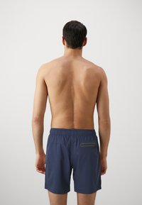 Navy swim shorts with an elastic waistband and a small zippered pocket on the back. Smooth fabric, mid-thigh length, minimalist design.