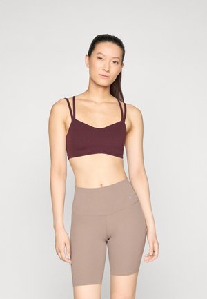 Bordeaux sportbeha met dunne schouderbanden, gecombineerd met tan high-waisted fietsbroekjes. Glad materiaal met een strakke pasvorm.