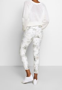 Biały, dziergany sweter o luźnym kroju. Spodnie o wąskim kroju w jasnych odcieniach z kwiatowym wzorem, z kieszeniami i metalicznymi akcentami. Białe trampki.