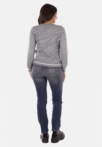 Maglione grigio con un motivo testurizzato, abbinato a jeans skinny blu scuro e stivali neri. Il maglione presenta un bordo e polsini a coste.