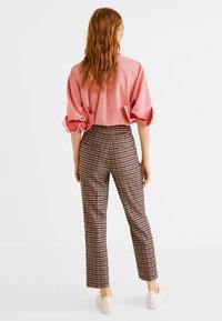 Lichtroze oversized shirt met pofmouwen, gecombineerd met hoogstaande bruine geruite broek en witte sneakers, gezien van de achterkant.