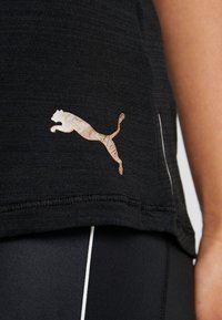 Svart atletisk topp med en texturerad tyg. Har en färgglad hoppande puma-logotyp och vita detaljer vid sömmarna. Närbild.
