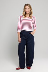 Rød- og hvidstribet langærmet top, højtaljede mørkeblå vide jeans og skinnende røde sko. Enkel, afslappet påklædning med synlige sømme.