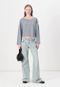 Camisa cinza de manga longa e corte curto, jeans de cintura alta azul claro desbotados, bolsa preta e sapatos pretos planos. Estilo simples, ajustado de forma descontraída.