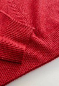 Red sweater with a soft texture, featuring ribbed cuffs and hem. Subtle pattern detail woven into the fabric. Cozy and warm appearance.