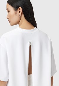 Witte top met korte mouwen, voorzien van een ritssluiting aan de achterkant en een uitsnede, gemaakt van een gladde stof. Strak ontwerp met een ronde halslijn.