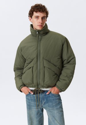 Giacca puffer verde oliva con colletto alto, zip frontale e polsini elasticizzati. Presenta due grandi tasche frontali e un orlo con cordino.