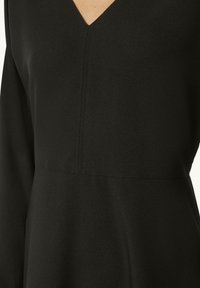 Schwarzes Kleid mit V-Ausschnitt, aus glattem Material gefertigt. Lange Ärmel und ein taillierter Körper mit Nähten schaffen eine minimalistische Silhouette.