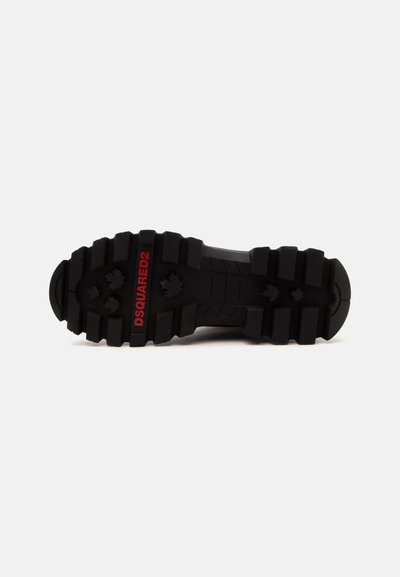 Semelle de chaussure noire robuste avec des rainures profondes et le logo rouge "DSQUARED2" sur fond blanc.