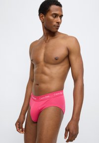 Ροζ βαμβακερά εσώρουχα με ελαστική μέση με λογότυπο. Ο σχεδιασμός έχει εφαρμοστή γραμμή και λεία υφή, τονίζοντας καθαρές γραμμές και ελάχιστες ραφές.