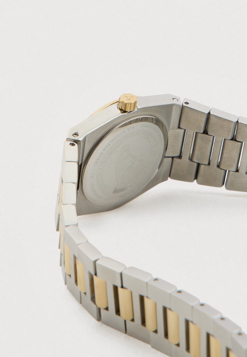 Zilverkleurige en goudkleurige metalen horlogeband met een gesloten horlogekast die de achterkant toont en een gouden kroon op een witte achtergrond.