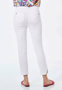 Weiße Jeans mit geradem Bein, Gesäßtaschen mit schwarzen Nieten und einer glatten Textur. Tragen mit rosa Sandalen.