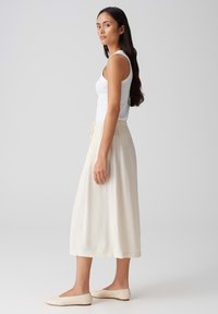 Jupe midi légère et fluide en crème avec une taille élastique et un cordon de serrage. Associée à un débardeur blanc ajusté et des ballerines beiges.