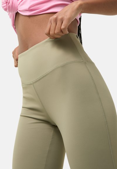 Olijfgroene, high-waisted leggings van een gladde, rekbare stof. Kenmerkt zich door platte naden en een brede tailleband voor comfort. Close-up weergave.