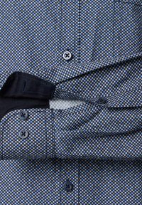 Schmal geschnittenes Hemd mit kleinem Karo-Muster in Blau, Weiß und Beige, schwarzem innerem Kragen und dunklen Knöpfen an Ärmeln und Vorderseite.