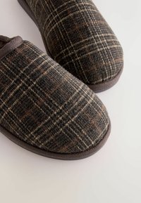 Kariertes Wollschlafzeug in Brauntönen und Grautönen, mit abgerundeten Zehen und einer weichen Textur sowie einem dunklen Stoffbesatz am Öffnungsrand.