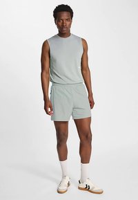Lysgrå atletisk tanktop og matchende shorts. Outfitet har en glat tekstur, elastisk taljebånd og diskret branding på toppen.