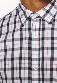 Camicia a quadri con bottoni, caratterizzata da motivi in plaid nero, bianco e rosso; colletto classico; bottoni bianchi; materiale in cotone.