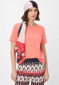 Coral short-sleeve t-shirt paired with patterned trousers featuring geometric designs in red, pink, and navy, complemented by a vibrant patterned scarf.