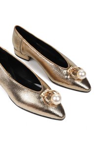 Złote metaliczne płaskie buty o teksturowanym wykończeniu, ze spiczastym noskiem, małym blokowym obcasem oraz ozdobnym akcentem perłowym z detalem w postaci złotego pierścienia.