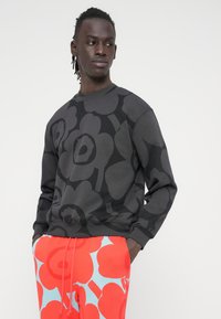 Μαύρο φούτερ με μεγάλο λουλουδάτο σχέδιο, συνδυασμένο με παντελόνι σε έντονο κόκκινο χρώμα με μπλε ανθικά σχέδια. Και τα δύο από απαλό ύφασμα.