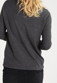 Gray long-sleeve knit sweater with a relaxed fit and ribbed hem, paired with black pants, showing soft texture and casual design.