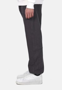 Charcoal gray sweatpants with a relaxed fit, featuring side pockets and pinstripe accents, paired with white Nike sneakers.