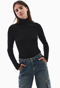 Czarny golf z długimi rękawami, teksturowana tkanina, zestawiony z jasnoniebieskimi, wysokim stanem spodni cargo z kieszeniami.