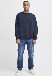 Marineblauwe sweatshirt met een ronde hals, geribbelde boorden en onderkant, gecombineerd met lichtblauwe jeans en witte sneakers. Eenvoudig, casual ontwerp.