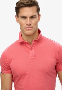 Polo shirt rossa in cotone con colletto corto, pattina con due bottoni e maniche corte. Texture liscia con un design aderente.