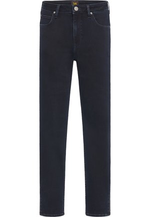 Person wearing olive green button-up shirt, dark skinny jeans, and black ankle boots, standing against plain gray background.