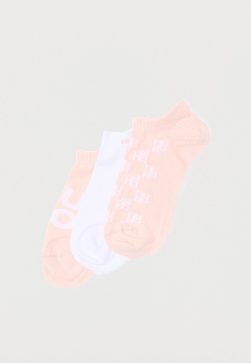 Τρία ζευγάρια κάλτσες χαμηλού κόψιμου σε ροδακινί και λευκό χρώμα, δύο ζευγάρια ροδακινί έχουν λευκό κείμενο τυπωμένο στις σόλες, τοποθετημένα δίπλα-δίπλα.