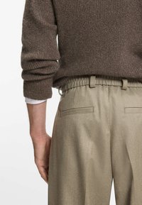 Bruine textuurtrui met opgerolde mouwen, gecombineerd met lichtbeige broeken met een elastische tailleband en twee achterzakken.