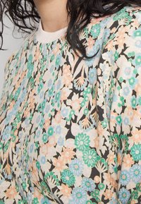 Haut à motifs floraux en tissu mélangé coton. Couleurs comprenant bleu clair, vert et pêche sur un fond noir. Encolure ronde.