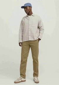 Light plaid button-up shirt with a pocket, beige chinos, and beige sneakers with white accents. Blue cap completes the outfit.