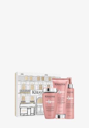 Juego de productos para el cabello Kérastase en un embalaje rosa y plateado, que incluye un tarro redondo y dos tubos, presentado en una caja decorativa con una ilustración parisina.