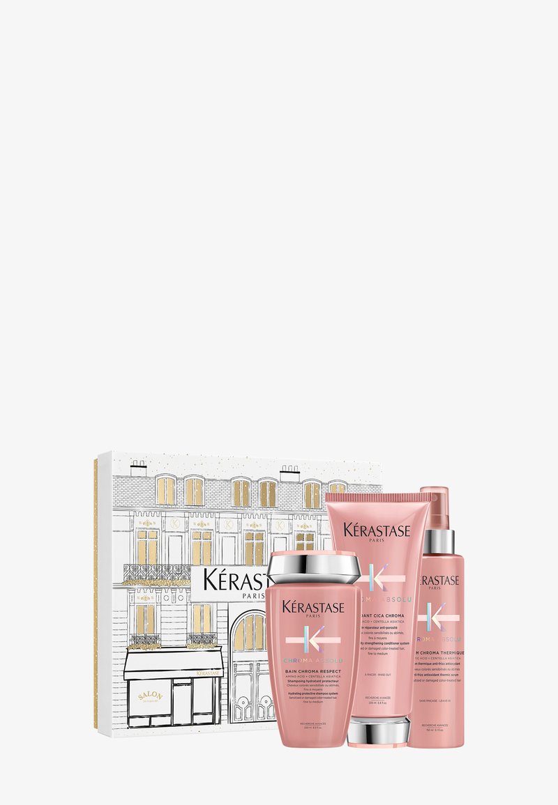 Zestaw pielęgnacyjny Kérastase w różowo-srebrnym opakowaniu, zawierający okrągły słoik i dwie tubki, zaprezentowany w dekoracyjnym pudełku z paryską ilustracją.