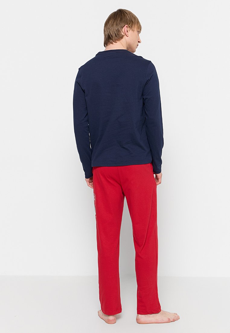 Maglietta a maniche lunghe navy abbinata a pantaloni rossi. La maglietta presenta un design semplice, mentre i pantaloni hanno un accento decorativo a motivo lungo il lato.