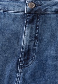Jean en denim de lavage foncé avec un léger éclat, présentant une poche avant, des coutures contrastantes et un bouton en métal à la taille.