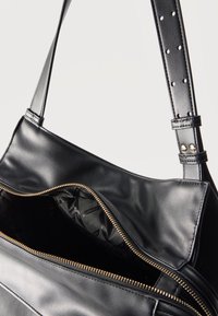 Μαύρη δερμάτινη τσάντα ώμου με χρυστό φερμουάρ που είναι μερικώς ανοιχτό, ρυθμιζόμενο λουράκι με πολλαπλές τρύπες και εσωτερική επένδυση από μαύρο ύφασμα.