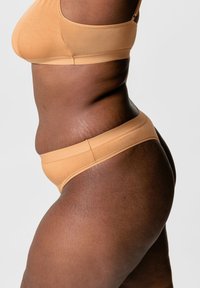 Naadloze nude bh en string set gemaakt van zachte, rekbare stof. De bh heeft een ronde halslijn en de string heeft een smalle tailleband.