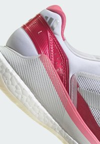 Jasnoszare sneakersy z teksturowaną cholewką, różowymi akcentami i połyskującym czerwonym wsparciem pięty. Elastyczna, wyściełana biała podeszwa dopełnia całość.
