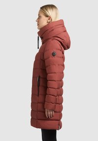 Rød dunjakke med en tætsiddende silhuet, høj krave og justerbar hætte. Har en sidelomme med lynlås og struktureret quiltet design.