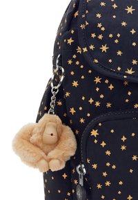Plecak z granatowej tkaniny, ozdobiony złotymi wzorami gwiazdek. Do plecaka przymocowany jest breloczek w kształcie pluszowej małpki, o okrągłym kształcie i jasnej, puszystej teksturze.