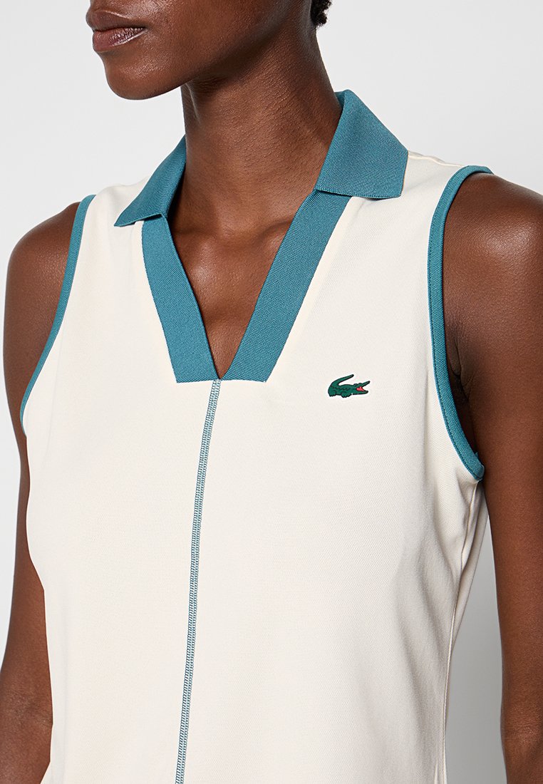 Ärmelloses Poloshirt in Creme mit einem türkisfarbenen Kragen. Mit einem Reißverschluss und dezentem Logo-Detail. Glattes Material mit tailliertem Design.