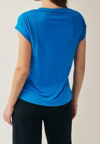 Niebieska koszula z krótkim rękawem o luźnym kroju, wykonana z gładkiej tkaniny. Projekt charakteryzuje się podwiniętymi rękawami i zakrzywionym dołem.