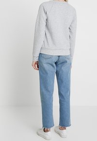 Sudadera gris clara con puños y dobladillo de canalé, combinada con jeans de mezclilla azules claros con dobladillo desgastado, y zapatillas blancas.