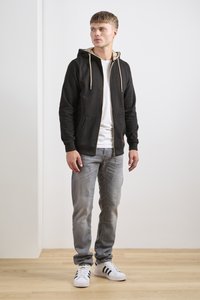 Musta vetoketjullinen huppari, jossa beigenvärinen vuori, etutaskut ja kiristysnyörit, yhdistetty vaaleansinisiin farkkuihin ja valkoisiin lenkkareihin. Taustalla puulattia.